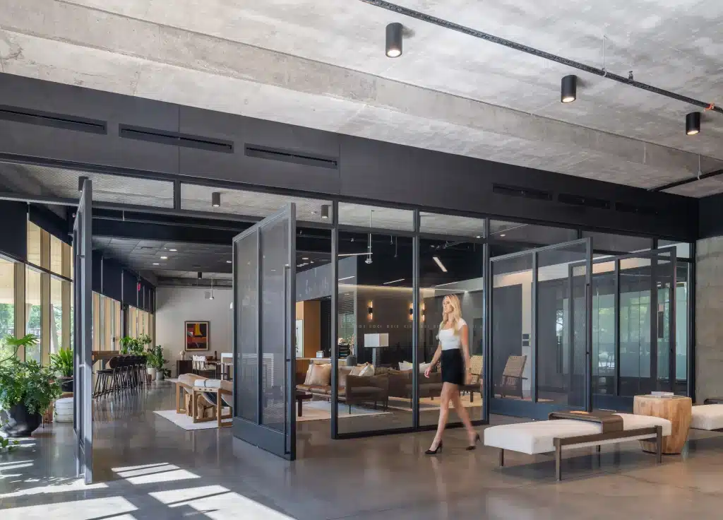 Glass-walled lounge at Eastbound in Austin, with large pivoting glass doors, an exposed concrete ceiling with track lighting and lounge seating