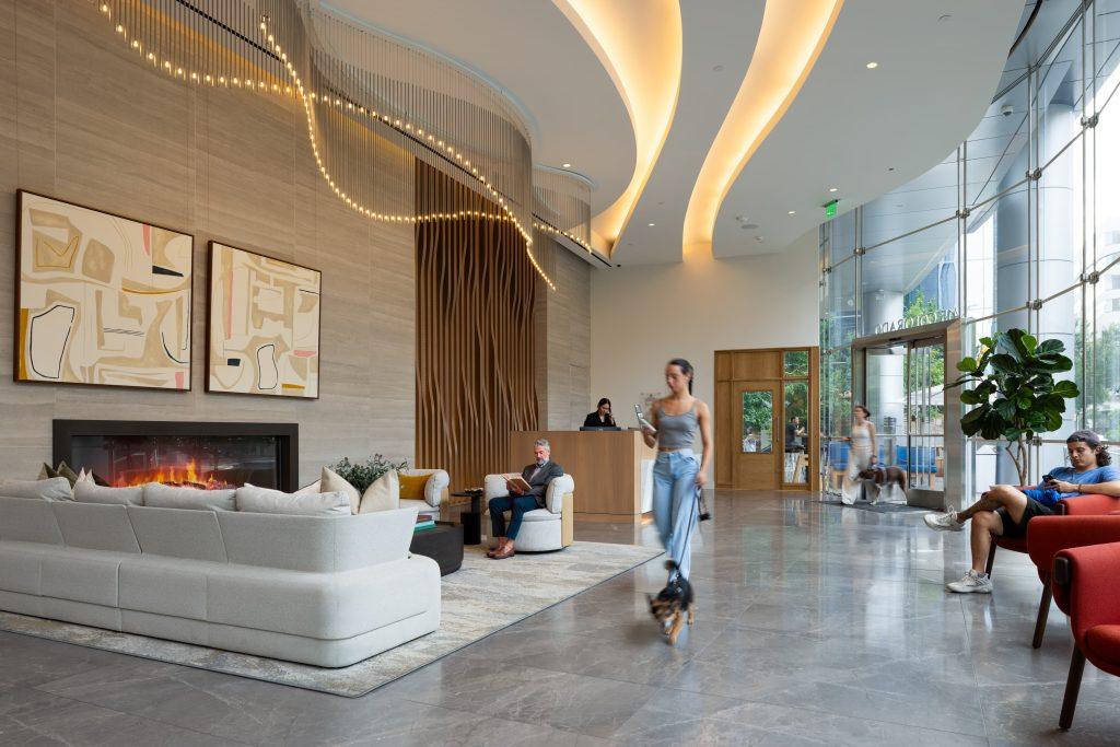 Lobby at 415 Colorado in downtown Austin, with a curving cove-lit ceiling, strands of suspended lights, a linear fireplace, abstract artwork and a wood-slat reception wall