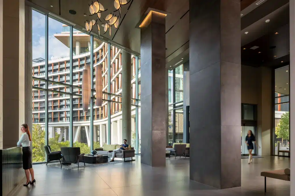 Double-height lobby at The Travis ATX in Austin, with floor-to-ceiling glass, a sculptural pendant chandelier, lounge seating and tall dark-clad columns