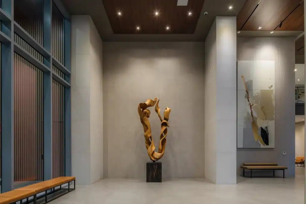 Lobby seating area at The Travis ATX in Austin, with a twisting golden sculpture on a dark plinth, large abstract artwork and long benches beneath a wood ceiling panel